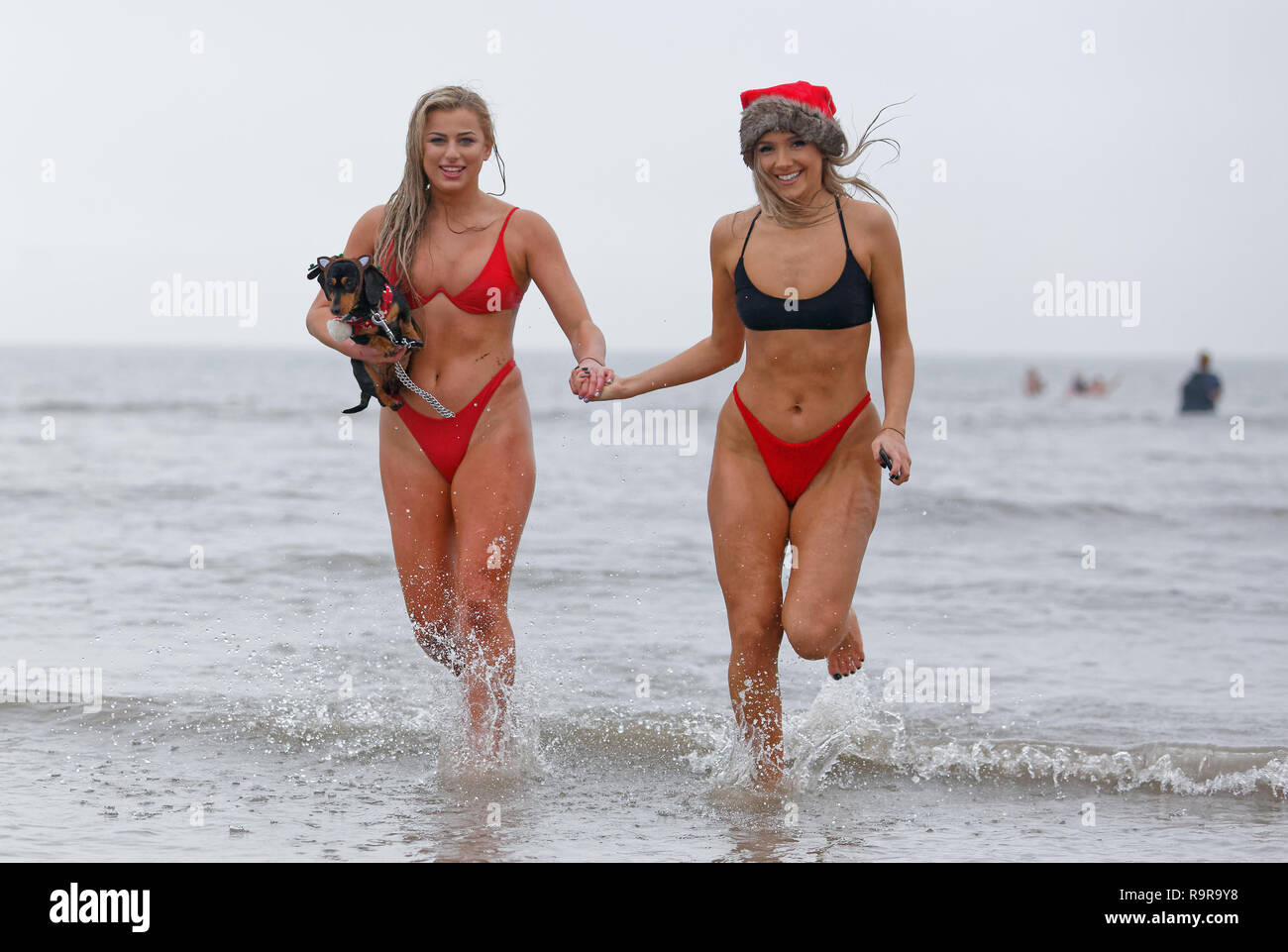 Pictured: Two young women in bikinis and Santa hats run in the sea.  Tuesday 25 December 2018 Re: Hundreds of people take part in this year's Porthcaw Stock Photo