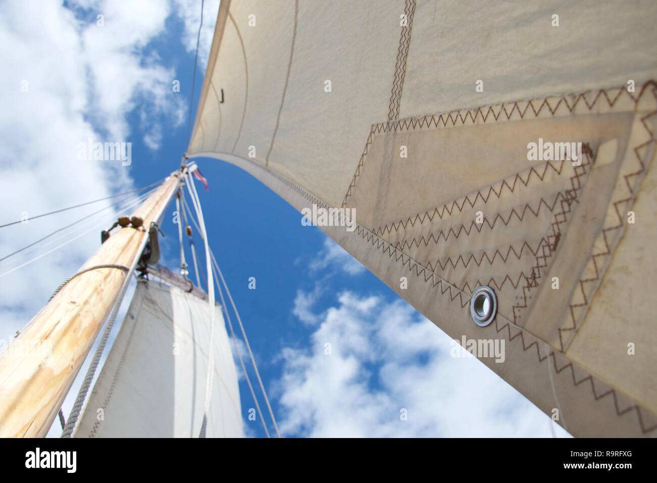 Looking up the mast on a traditional gaff rigged yacht / sailing boat. The focus is on an eyelet in the jib (smaller sail). The sky is blue with littl Stock Photo