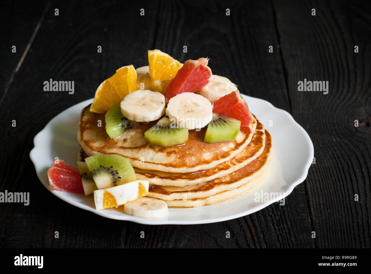 Plate of pancakes with fruits and honey at dark wooden table. Stock Photo