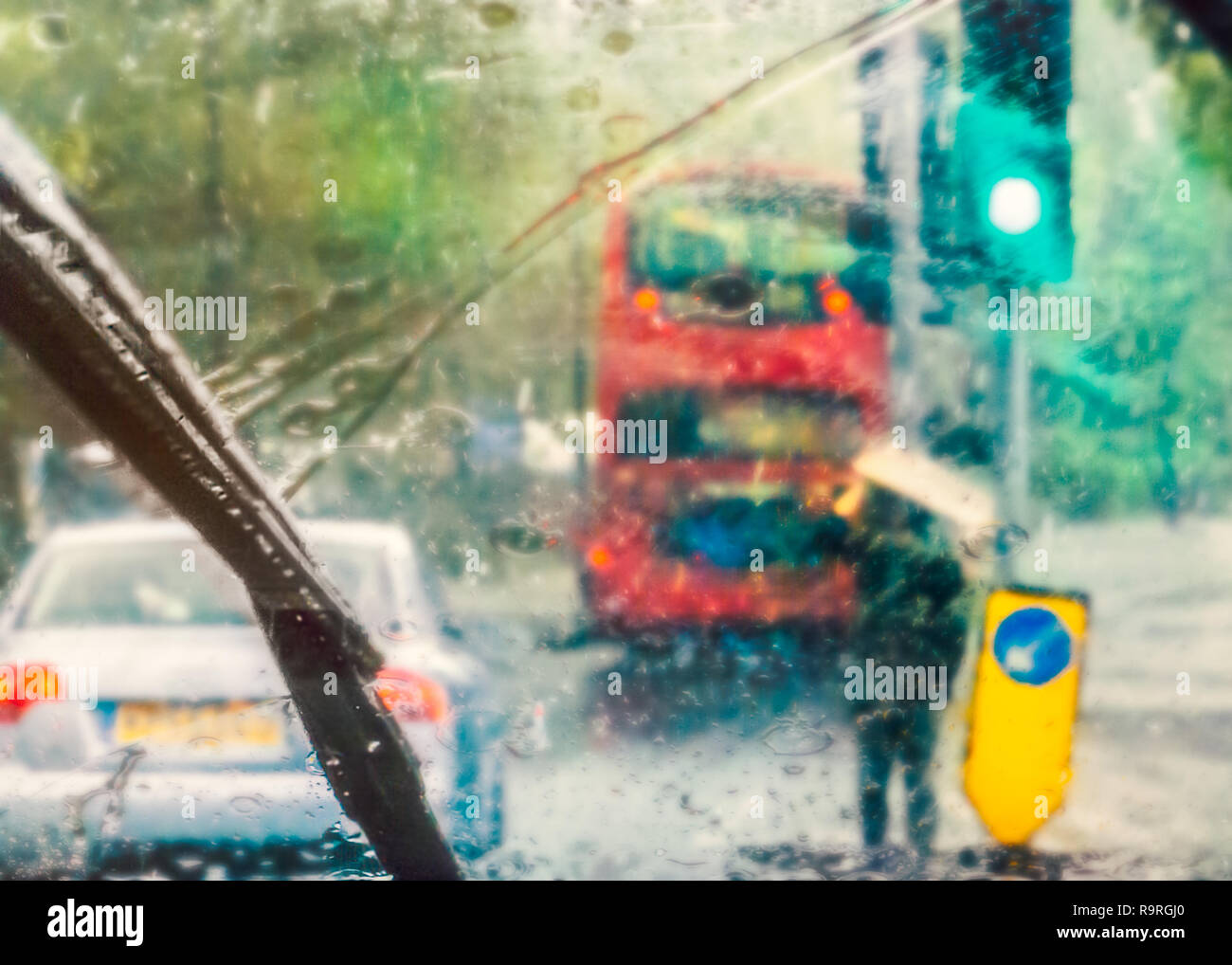 London street scene abstracted by rain on a car windscreen on a rainy day. A red bus can be seen and a man holding cardboard above his head for shelte Stock Photo