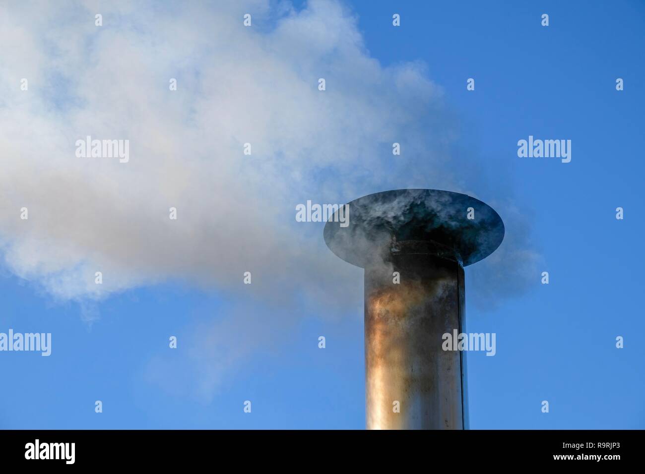 Smoke billows from the vent pipe of a stainless steel outdoor furnace. Stock Photo