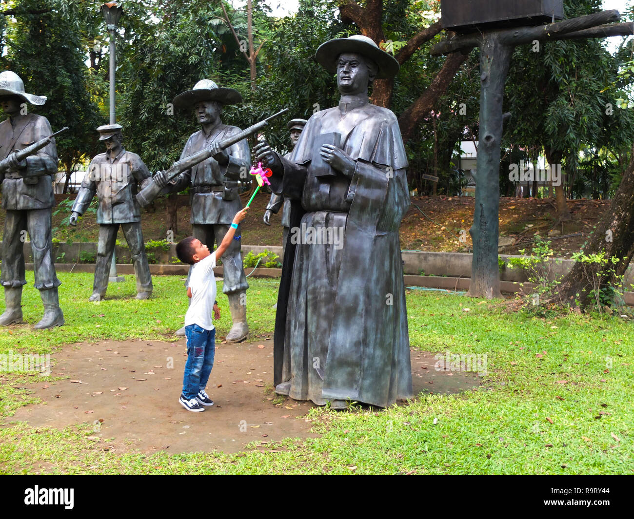 A kid raising up his toy at the bronze statue of a Spanish Friar at the