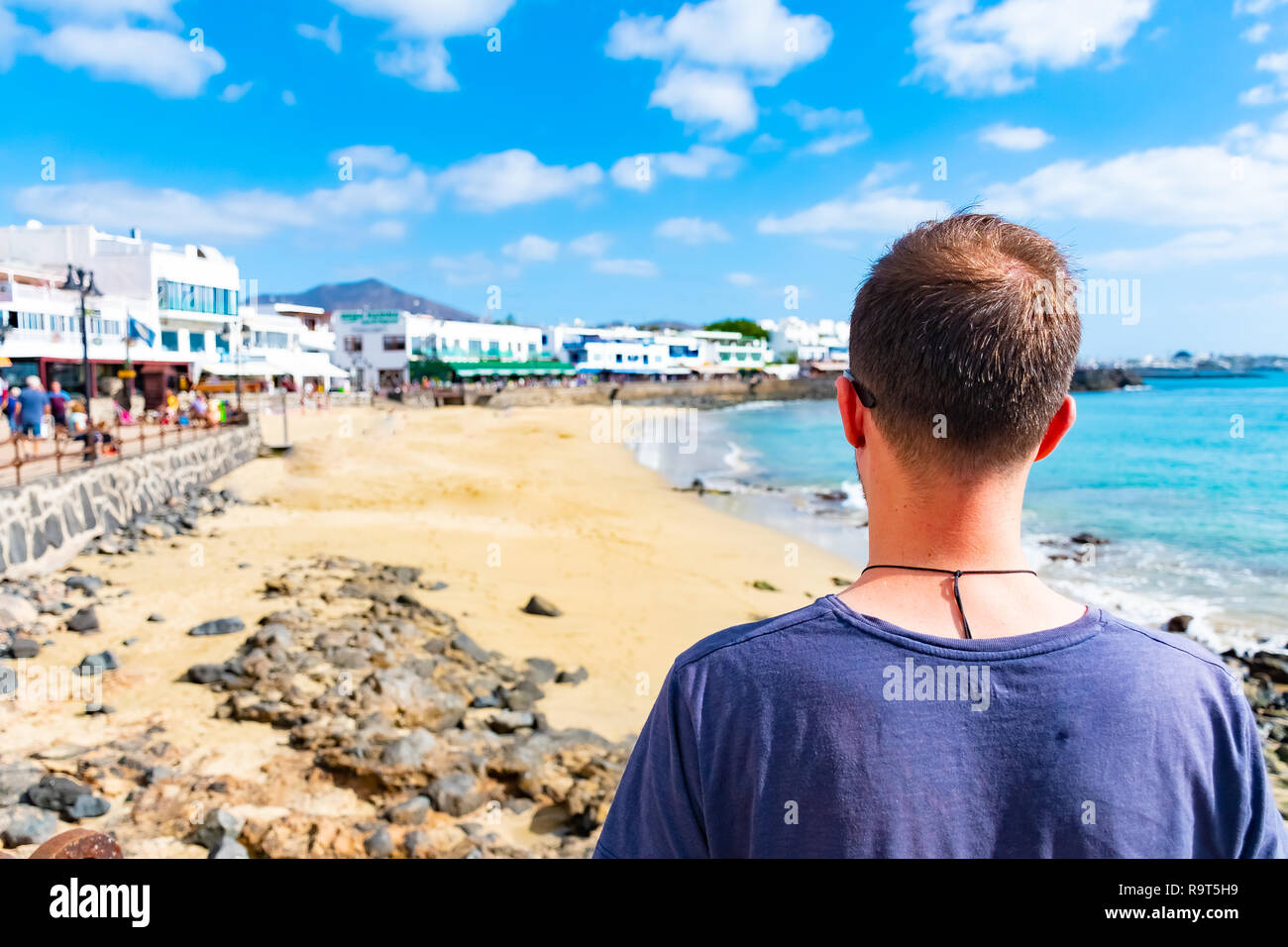 A man looking at seaside promenade in Playa Blanca, the former fishermens village became a main touristic spot with opening of the new harbor, Lanzaro Stock Photo