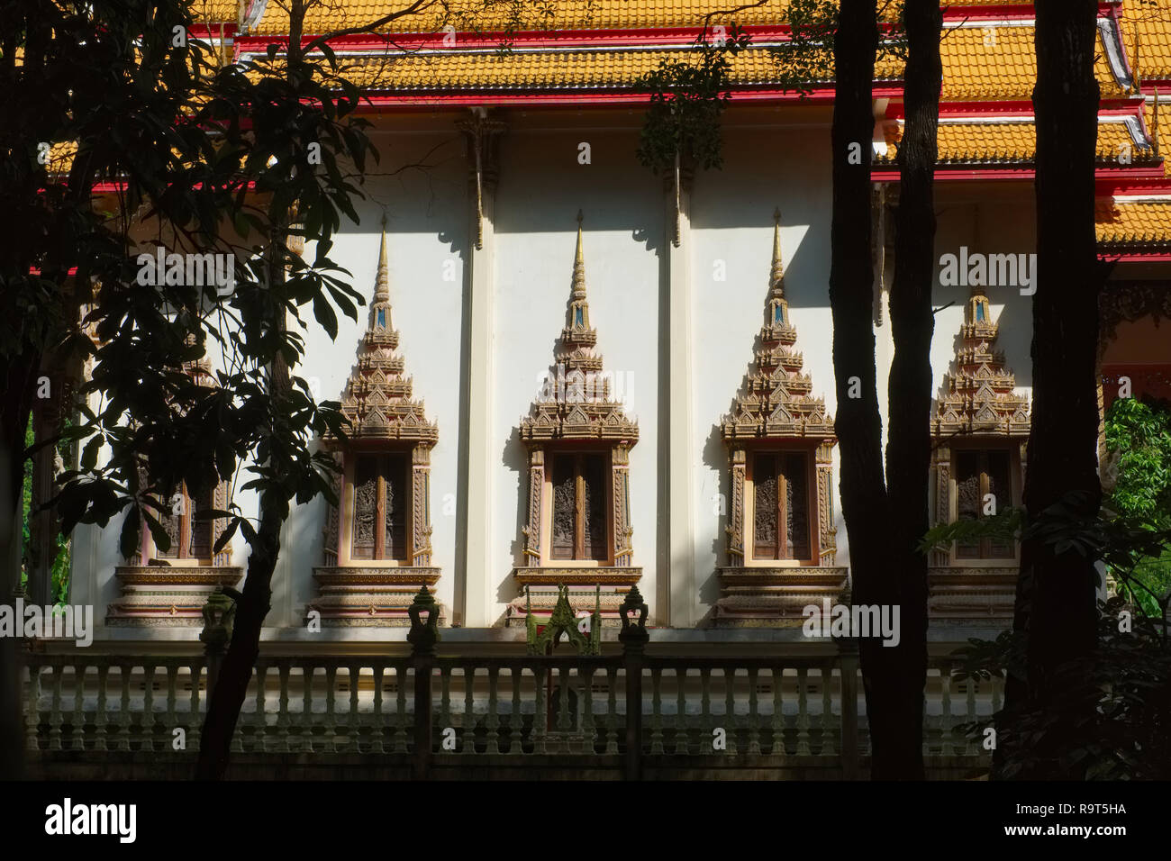 Ornate, elaborate windows in Wat Tha Ruea in Thalang, the former capital city of Phuket, Thailand, seen from the adjoining grove Stock Photo