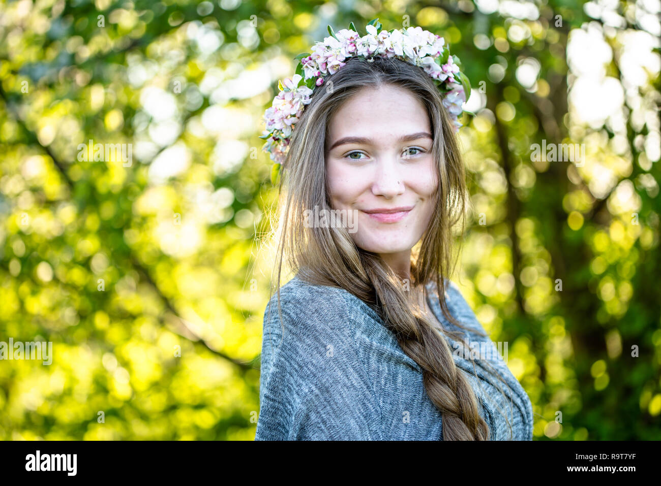 Natural beauty of smiling girl face with beautiful skin, braid and floral wreath on head. Young woman, spring portrait, outdoors Stock Photo