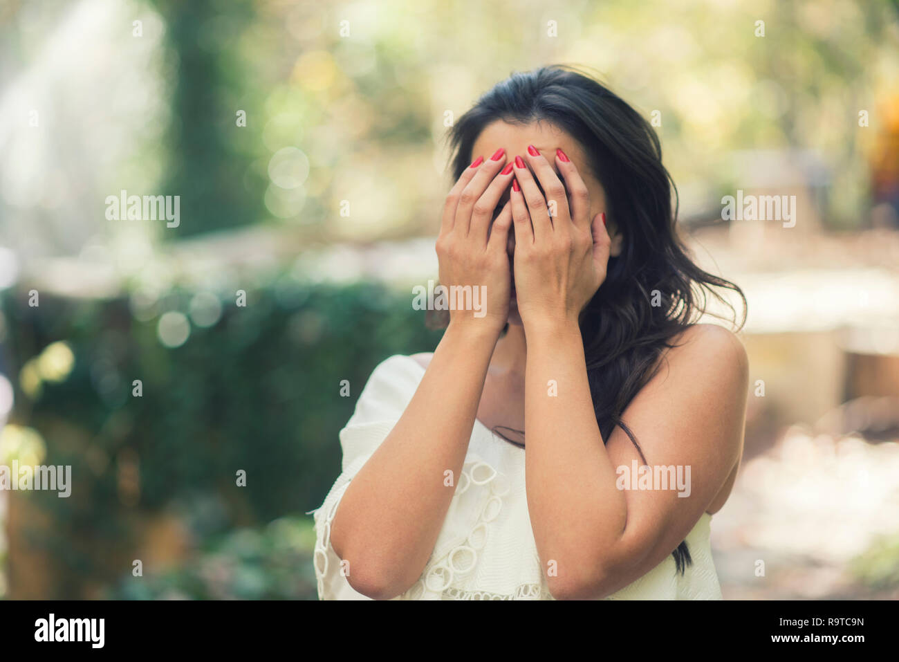 Young woman hands hiding face crying outdoors Stock Photo