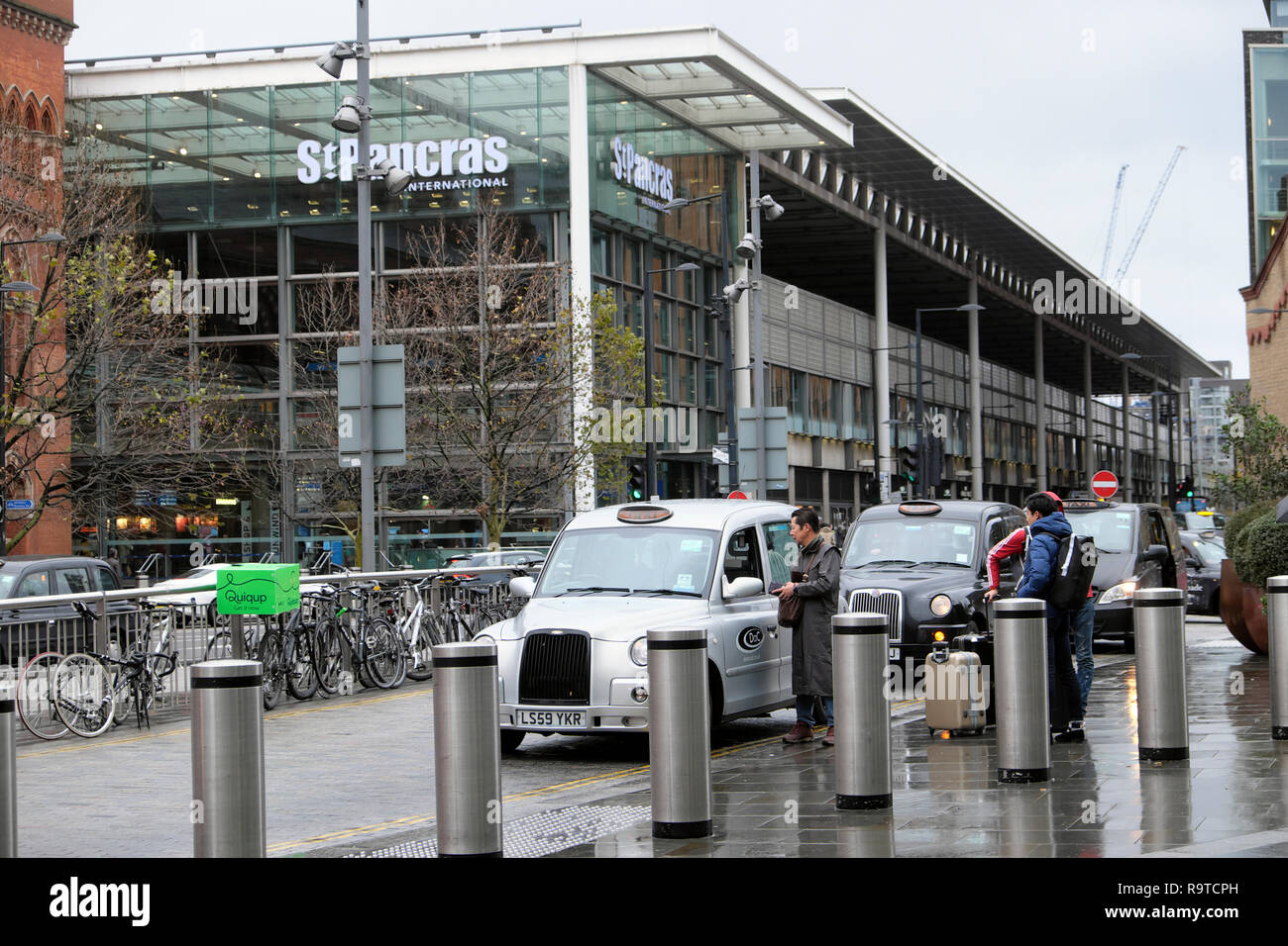 View passengers with luggage paying taxi driver at St Pancras Station building Pancras Road at