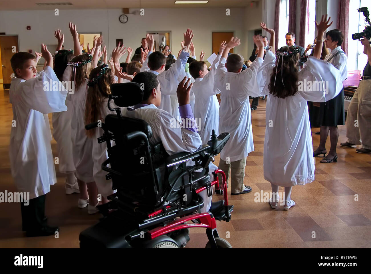 Middletown, CT USA. May 2009. Physically disabled young man in wheelchair looked on by a curious boy while participating in First Communion activities. Stock Photo