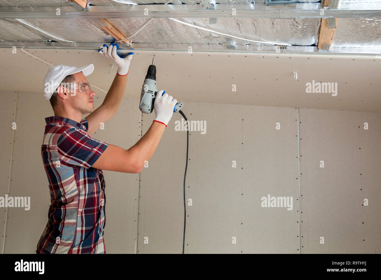 Young Man In Goggles Fixing Drywall Suspended Ceiling To Metal