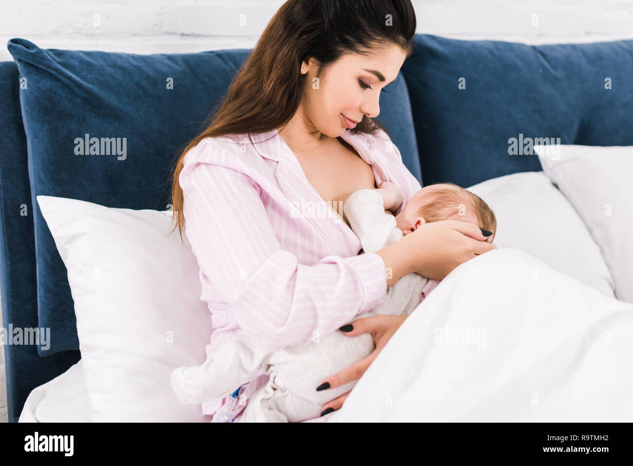 portrait of young mother breastfeeding little baby on bed at home Stock