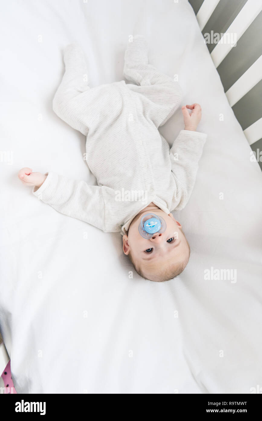 overhead view of little baby with pacifier lying in crib Stock Photo