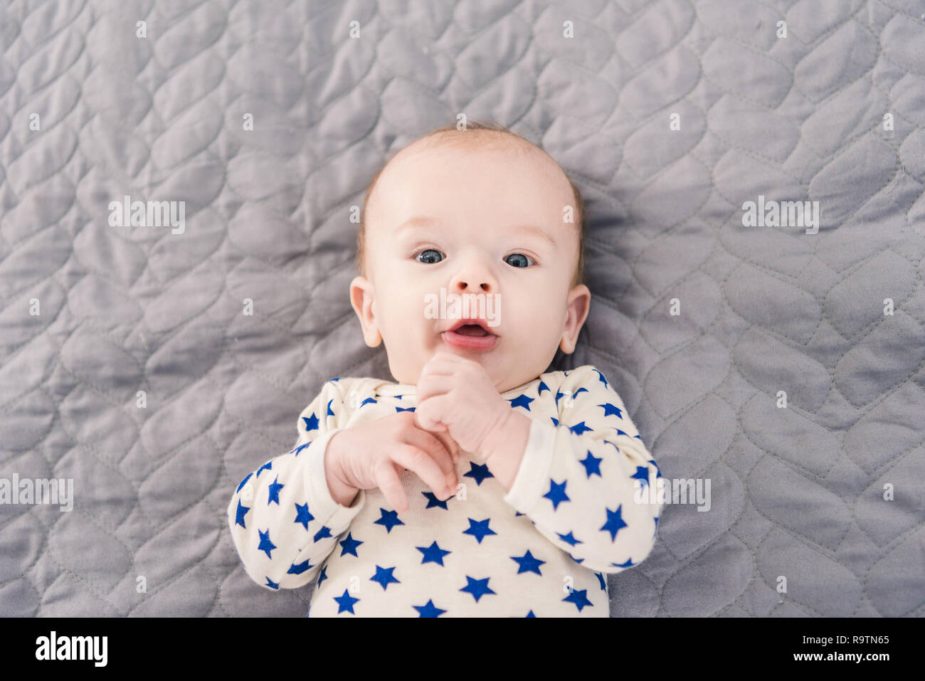overhead view of adorable little baby lying on grey blanket Stock Photo