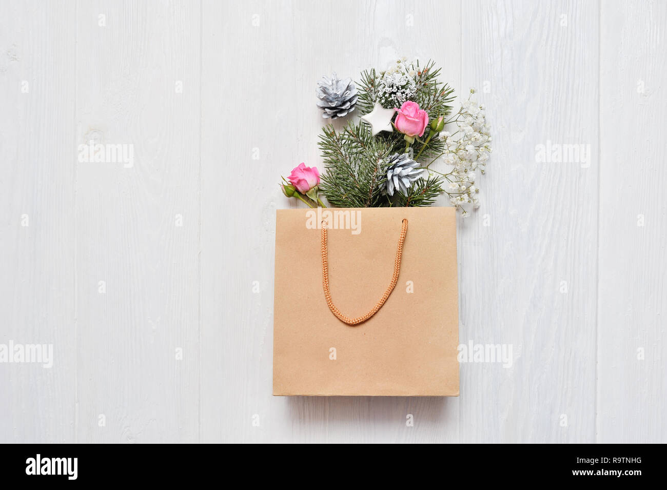 Christmas mockup. Kraft package with xmas decor fir branches, pink roses, cones with place for your text. Shopping concept Stock Photo