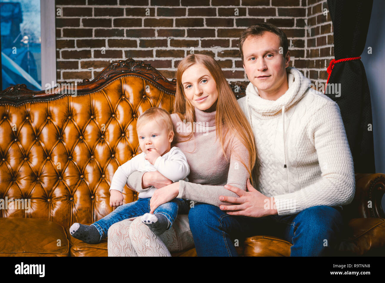 theme new year and Christmas holidays in family atmosphere. Mood celebrate Caucasian young mom dad and son 1 year old sit on a leather brown sofa at h Stock Photo