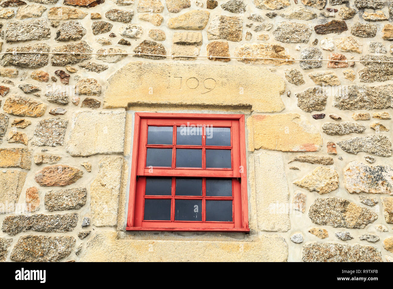 Red guillotine window on a stone framed window with date on top in the historic village of Linhares da Beira, Gouveia, Portugal Stock Photo