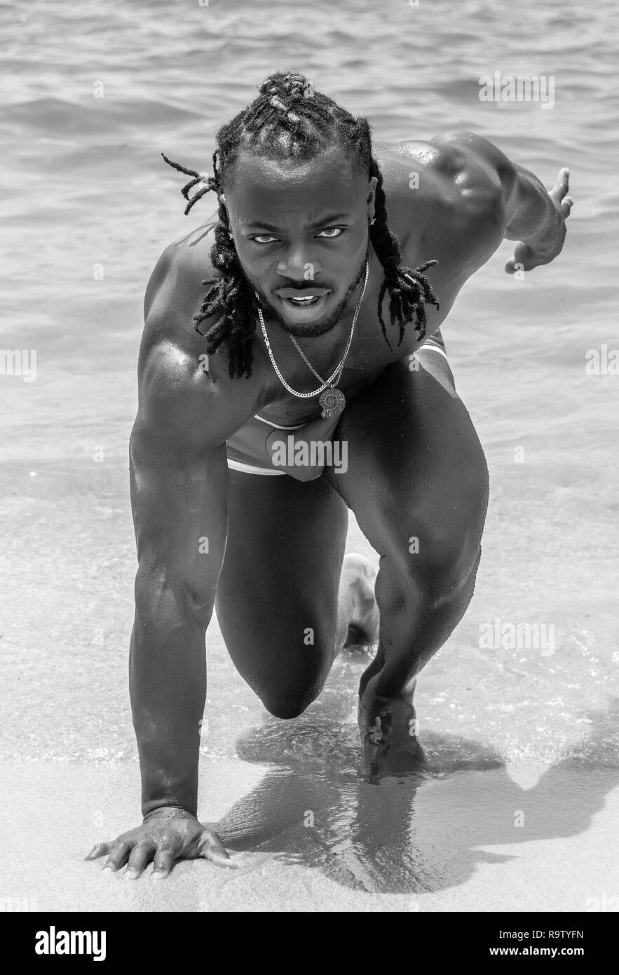 Black and white photo of a young, handsome, muscular, shirtless African American man posing with one of his knees in the send, on Yelapa beach near Pu Stock Photo