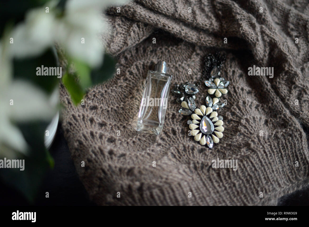 perfume bottle and a necklace on a knitted sweater by a white poinsettia flower Stock Photo