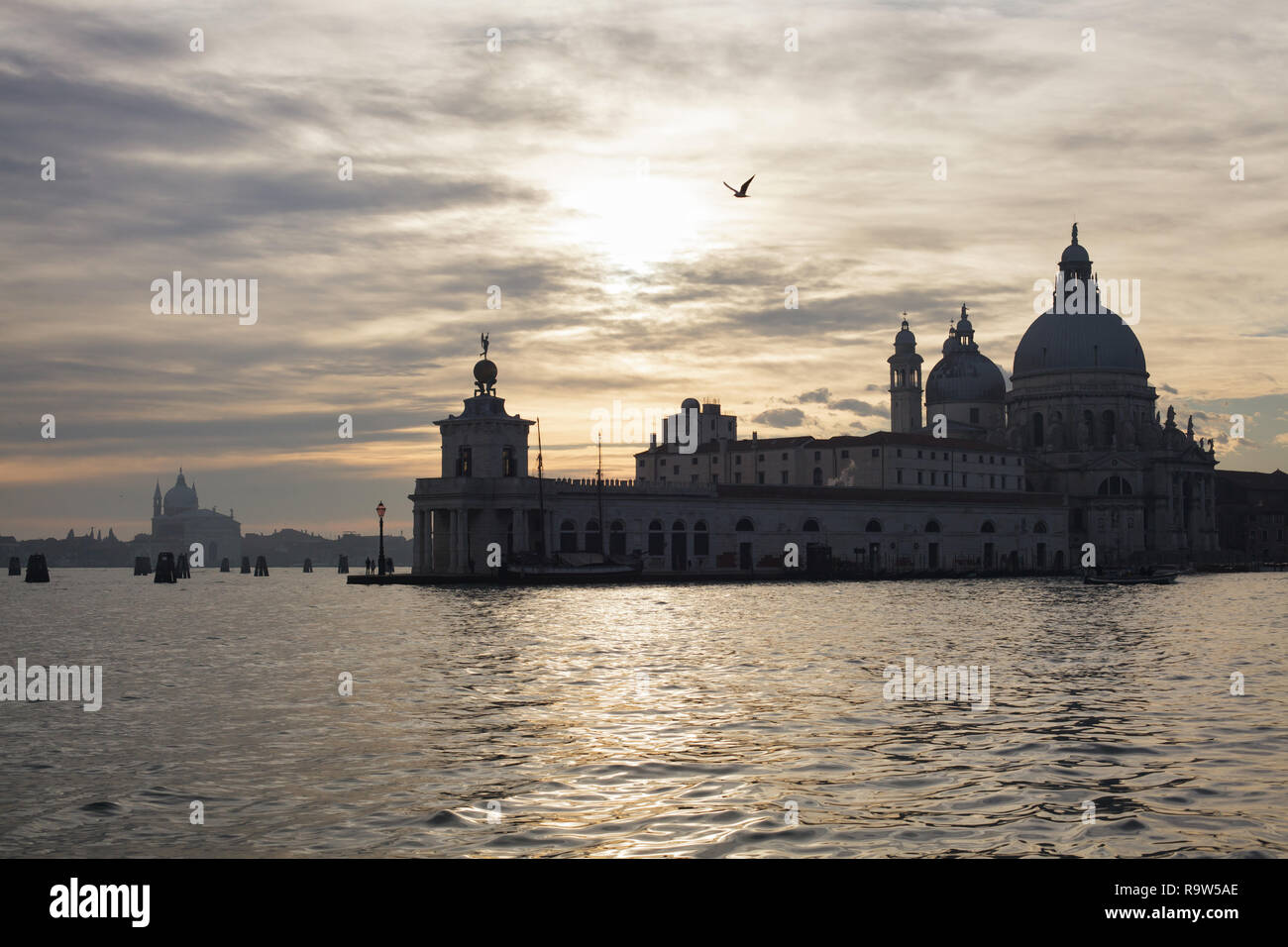 Sunset over the Punta della Dogana and the Basilica of Santa Maria della Salute (Basilica di Santa Maria della Salute) in Venice, Italy. The Redentore Church (Chiesa del Santissimo Redentore) on Giudecca is seen in the background. Stock Photo