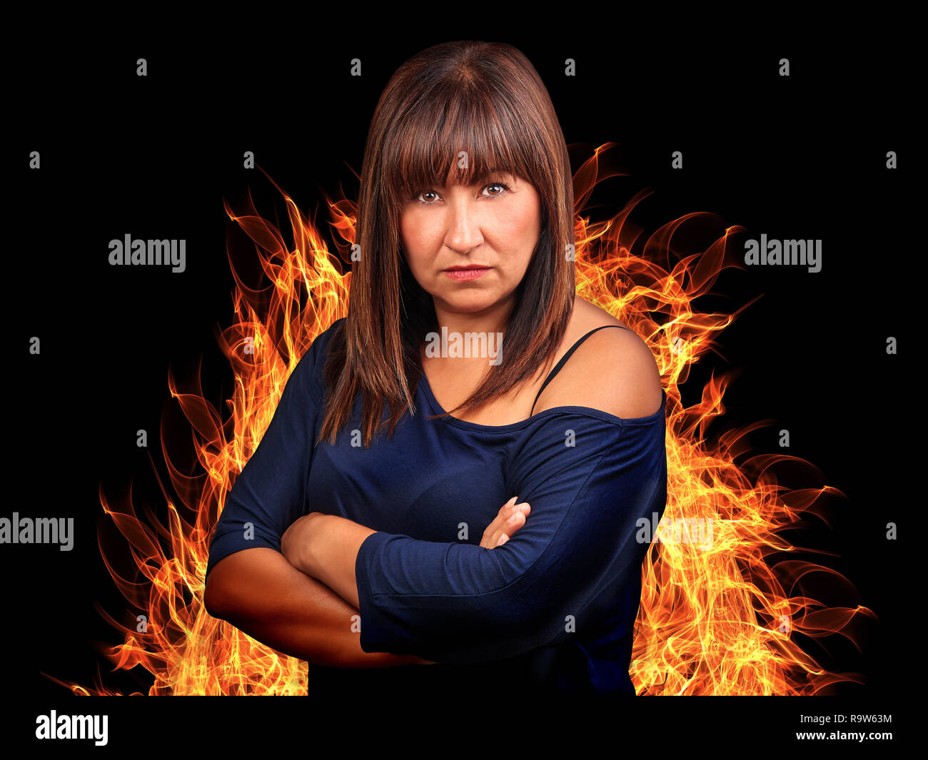 Brunette woman angry with crossed arms surrounding by fire Stock Photo