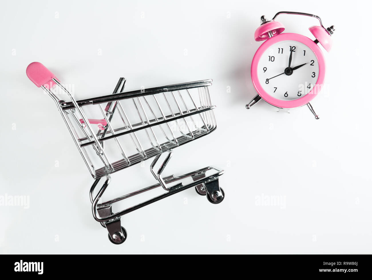 Female shopping time. Shopping cart and alarm clock pink color on a