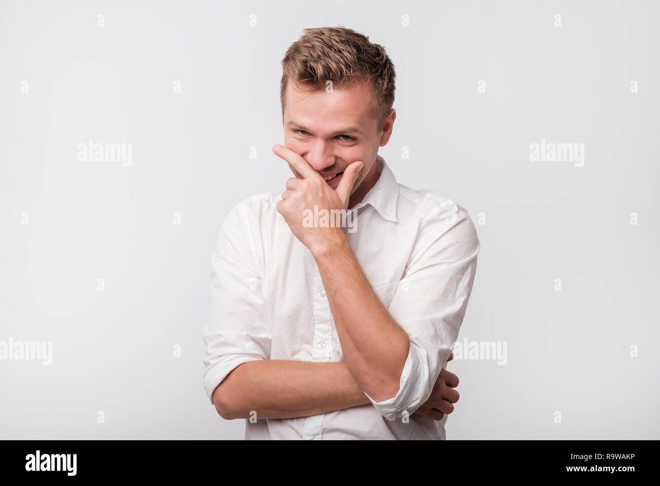 Mature man laughing and covering his mouth with hand over white background. Stock Photo
