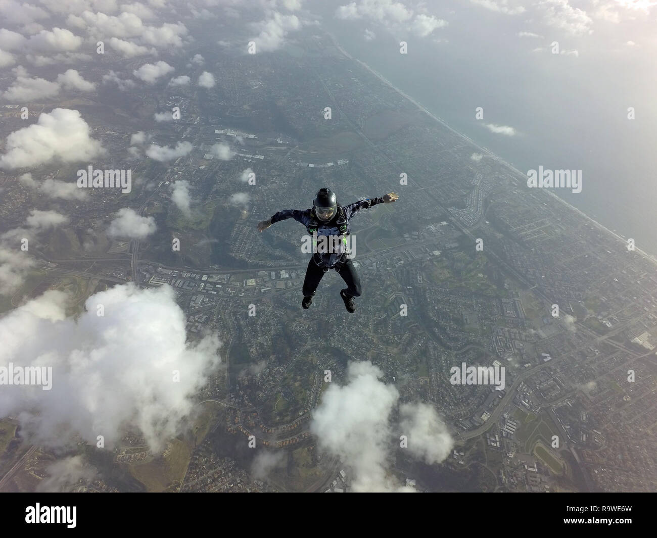 This freefly skydiver is practice different freestyle positions in the blue sky over some clouds with a big smile on his face. Stock Photo