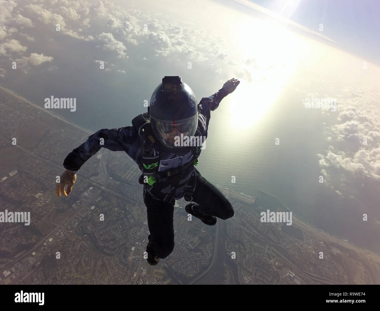 This freefly skydiver is practice different freestyle positions in the blue sky over some clouds with a big smile on his face. Stock Photo