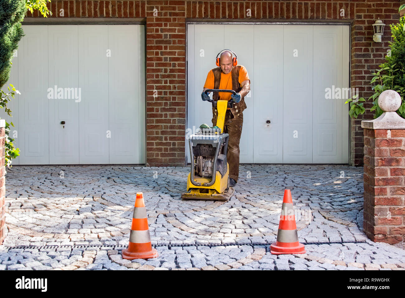 Builder or contractor laying new paving bricks in a house driveway using a mechanical compacter for compaction of the cement pavers. Stock Photo
