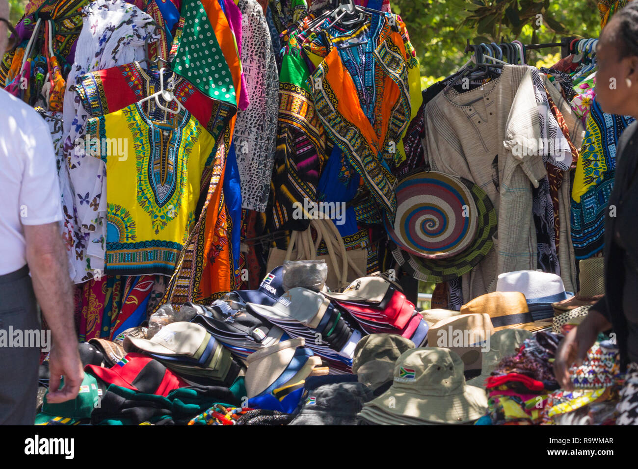 brightly coloured and vibrant African shirts or clothing hanging up and a variety of caps and hats displayed for sale in the street in Cape Town Stock Photo