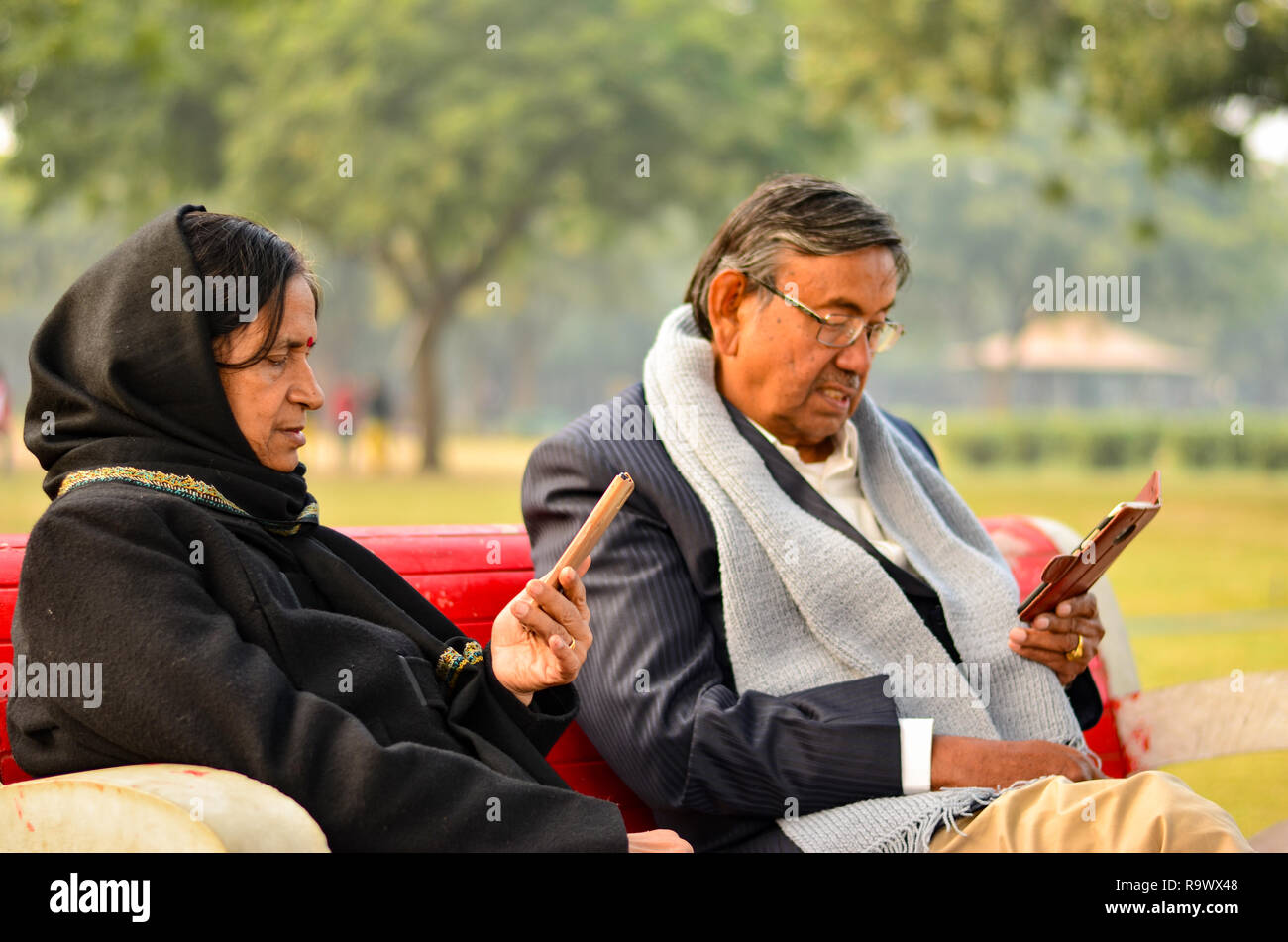 Senior couple sitting in park looking at the phone and smiling in Delhi ...