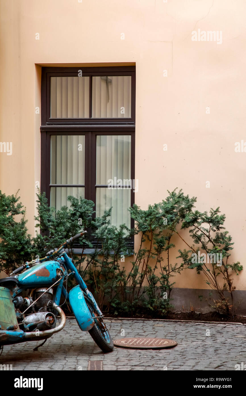 Fragment of beige wall with window in Old Riga, Latvia. Ancient motorcycle next to the wall. Stock Photo