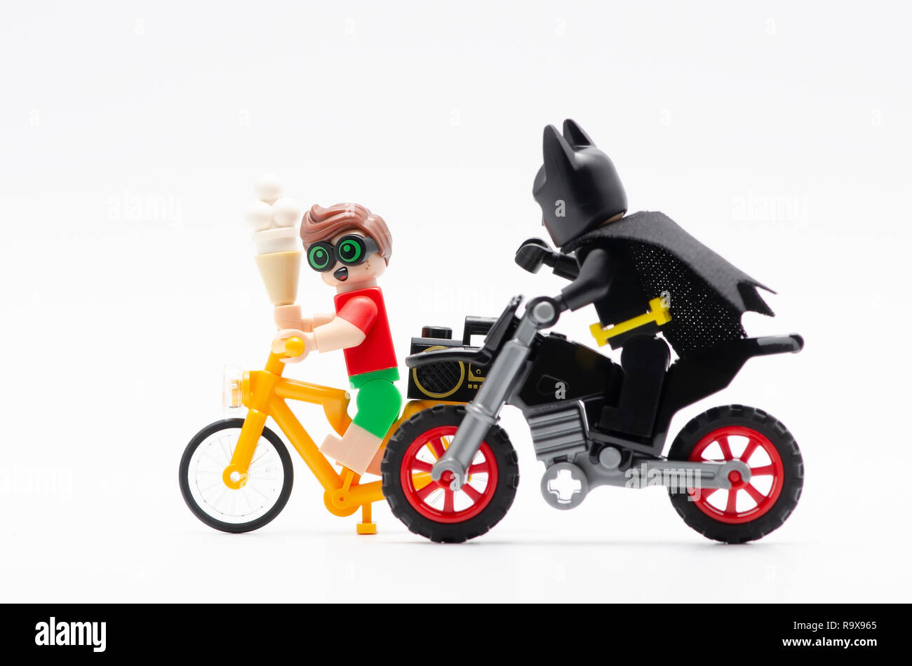 lego batman with robin riding bicycle with radio at his back and holding a ice cream. Lego minifigures are manufactured by The Lego Group. Stock Photo