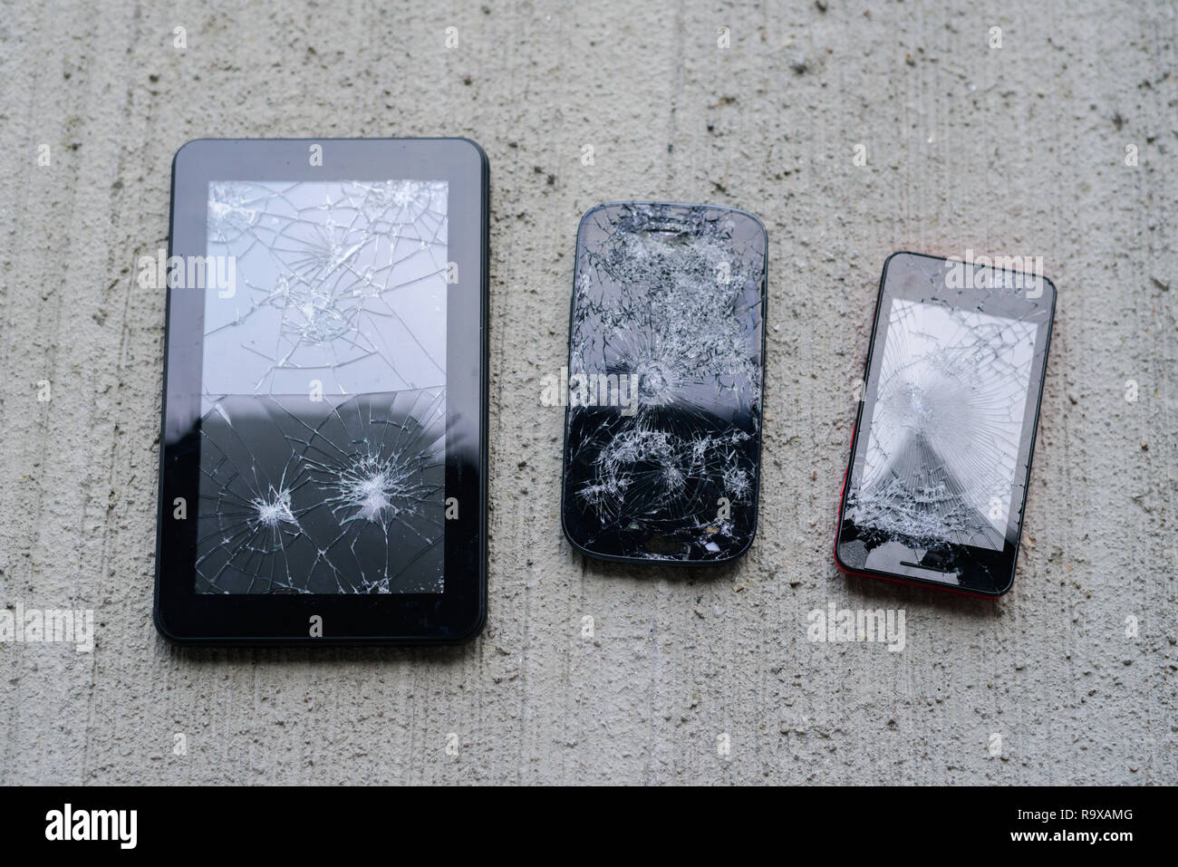 Broken phones and tablet on concrete background. Cracked screen Stock Photo