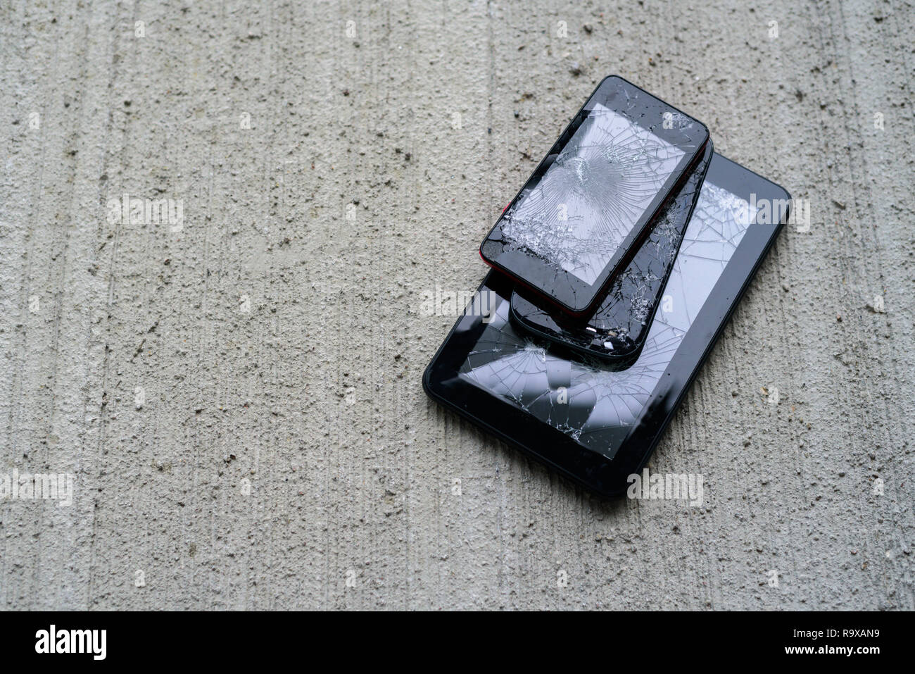Broken phones and tablet on concrete background. Cracked screen Stock Photo