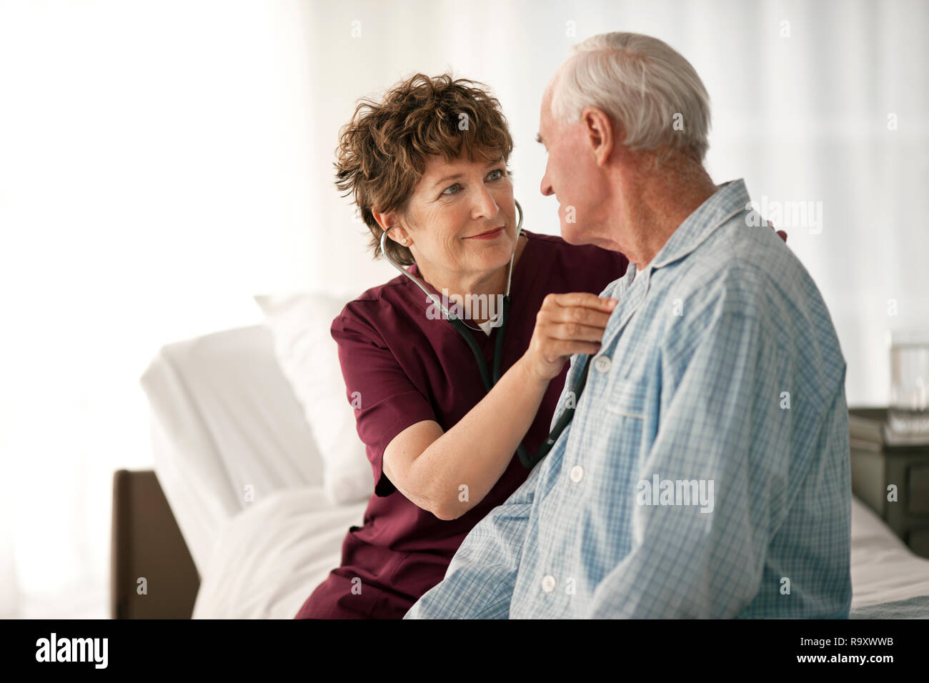 Mature nurse listening to the heartbeat of an elderly patient. Stock Photo