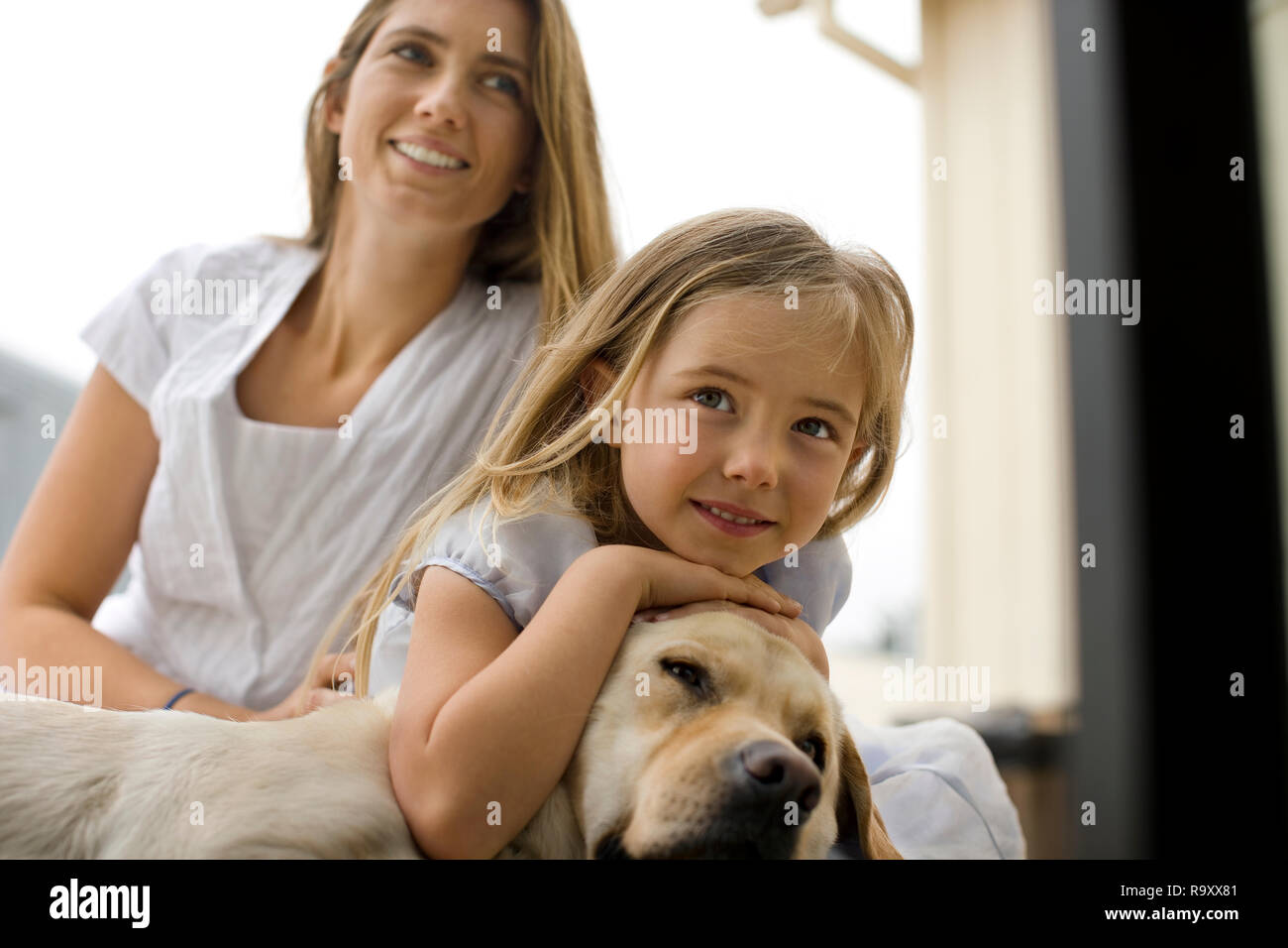 Little girl and her smiling mother relax on the floor with their sleepy dog. Stock Photo