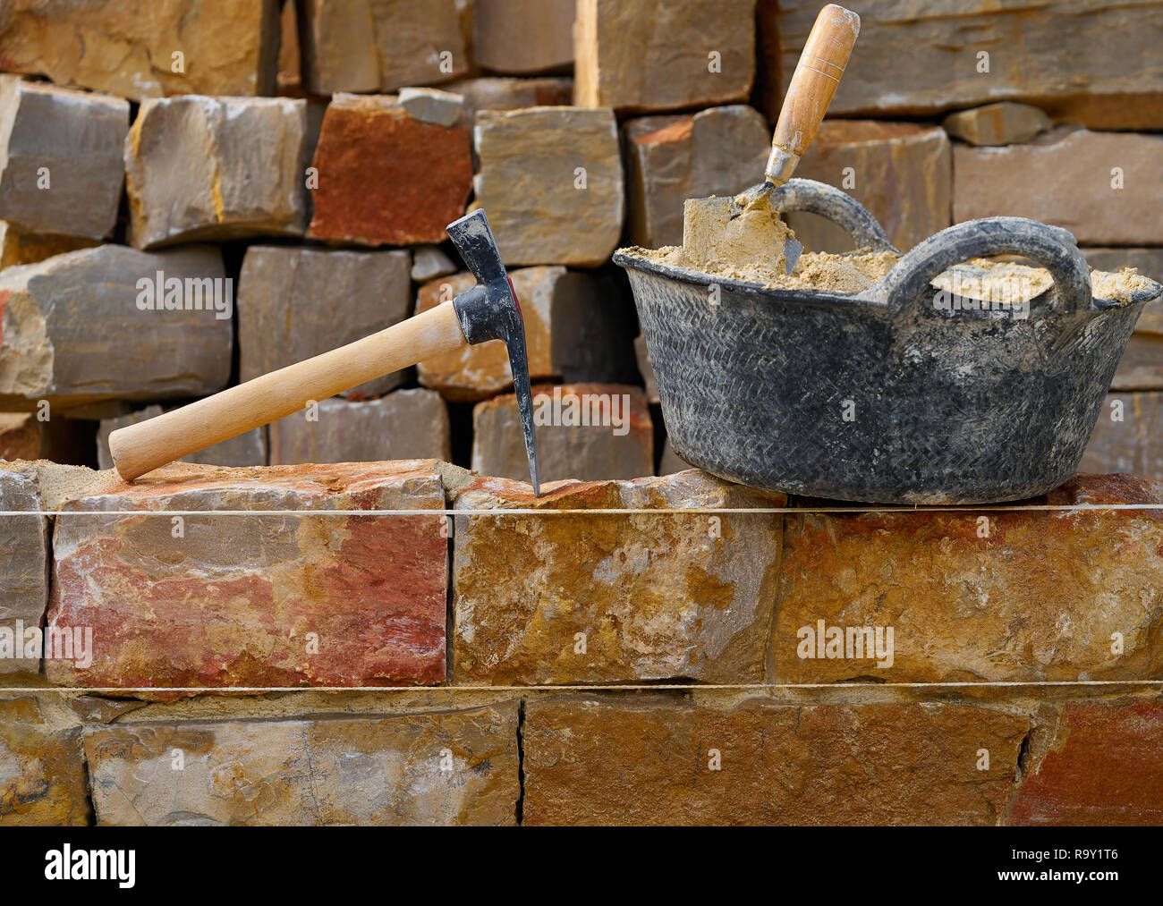 Masonry stone wall construction with mortar and brick hammer trowel