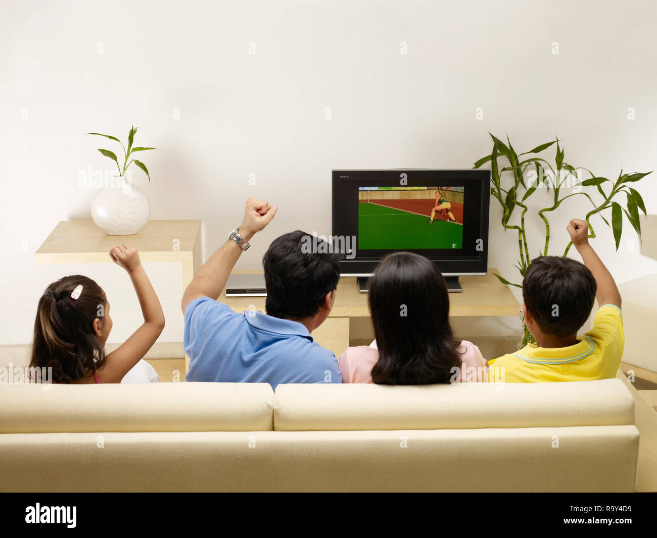 PORTRAIT OF FAMILY OF FOUR WATCHING TV IN THEIR HOME Stock Photo