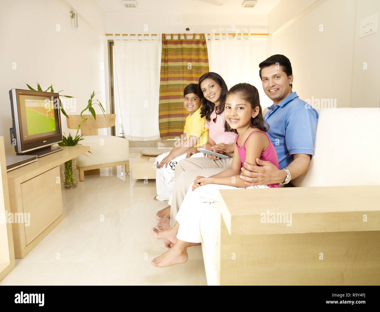PORTRAIT OF FAMILY OF FOUR WATCHING TV IN THEIR HOME Stock Photo