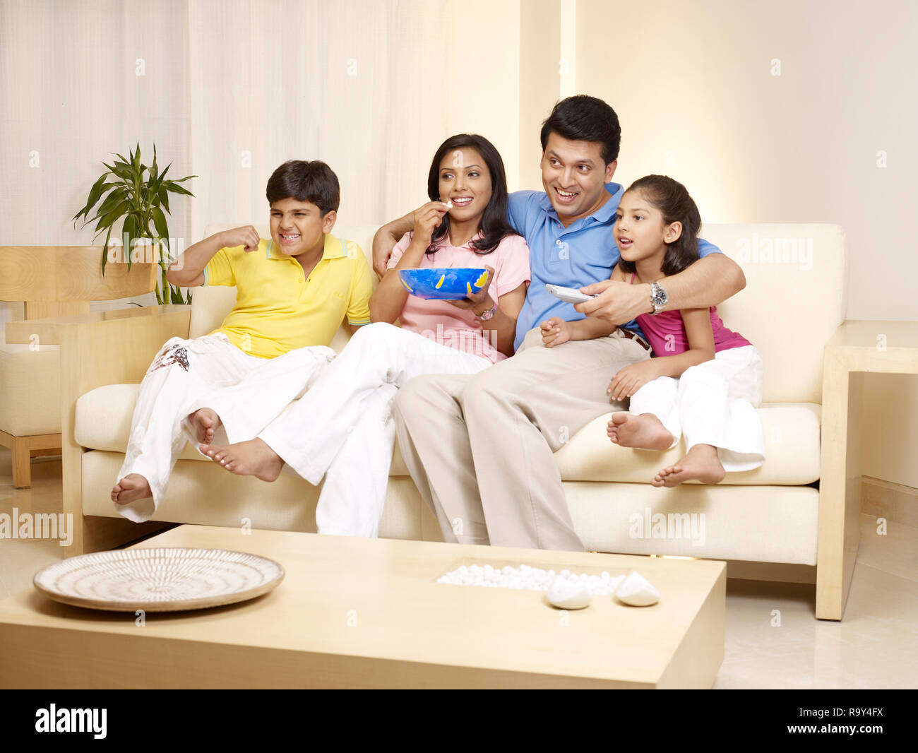 PORTRAIT OF FAMILY OF FOUR WATCHING TV IN THEIR HOME Stock Photo