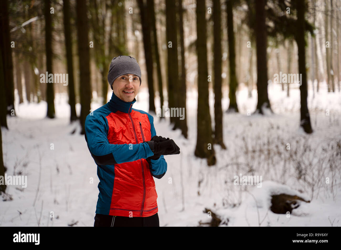 Runner wearing warm sporty clothes looks at a modern smart clock and counts up spent calories during winter training outdoors Stock Photo