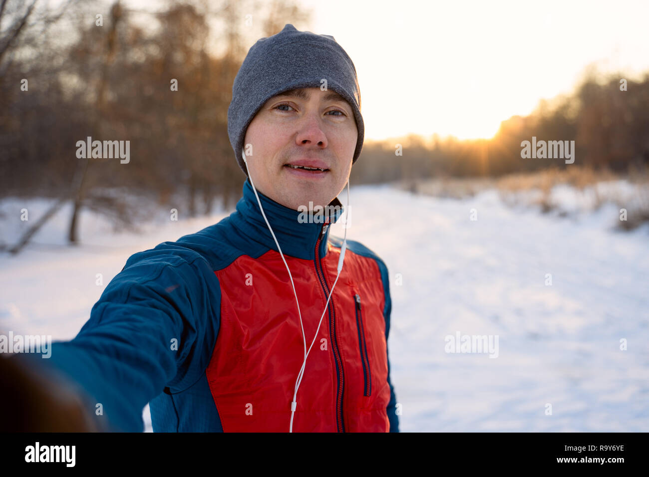 Runner wearing warm sporty clothes in headphones take selfie during winter training outdoors Stock Photo