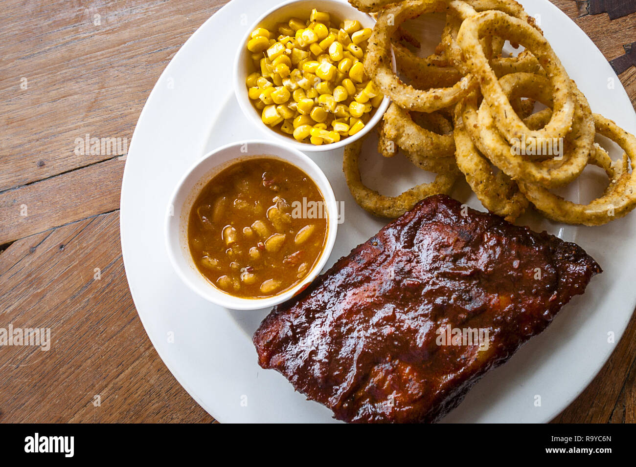 BBQ Ribs, baked beans, onion rings served on a white plate. Stock Photo