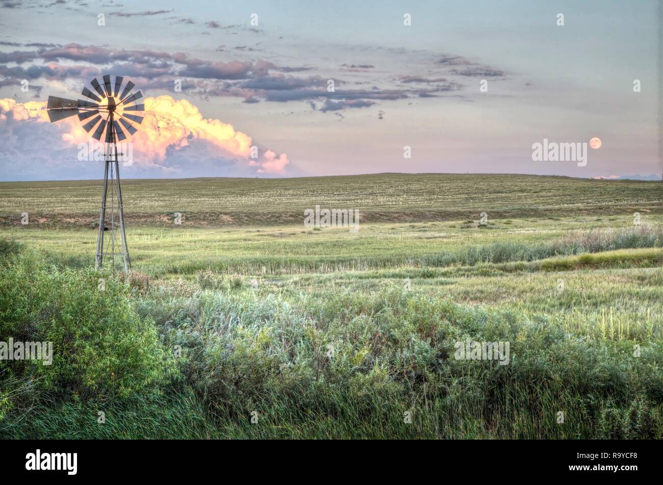 A Windmill On Colorado S Short Grass Prairie With A Background Of Clouds Lit By The Setting Sun And The Full Moon Rising Stock Photo Alamy