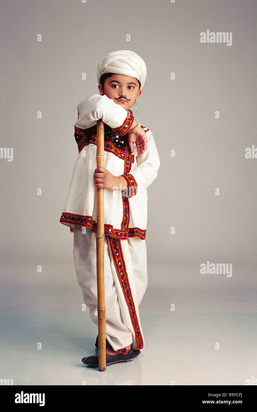 Yound Gujarati boy dressed as an adult famer wearing a 'kediu'with a false moustache, full figure with a stick Stock Photo