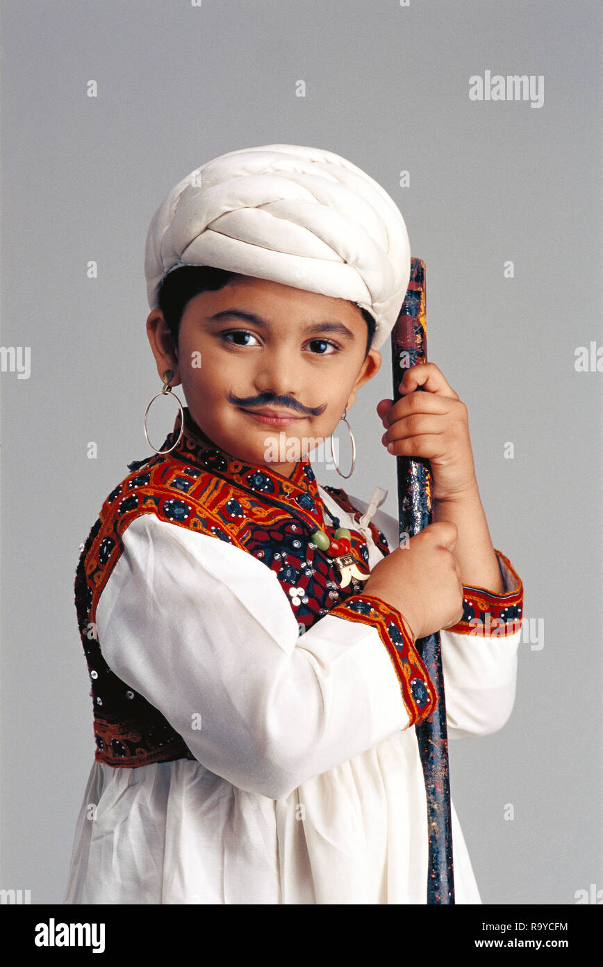 Yound Gujarati boy dressed as an adult famer wearing a 'kediu'with a false moustache, full figure with a stick Stock Photo