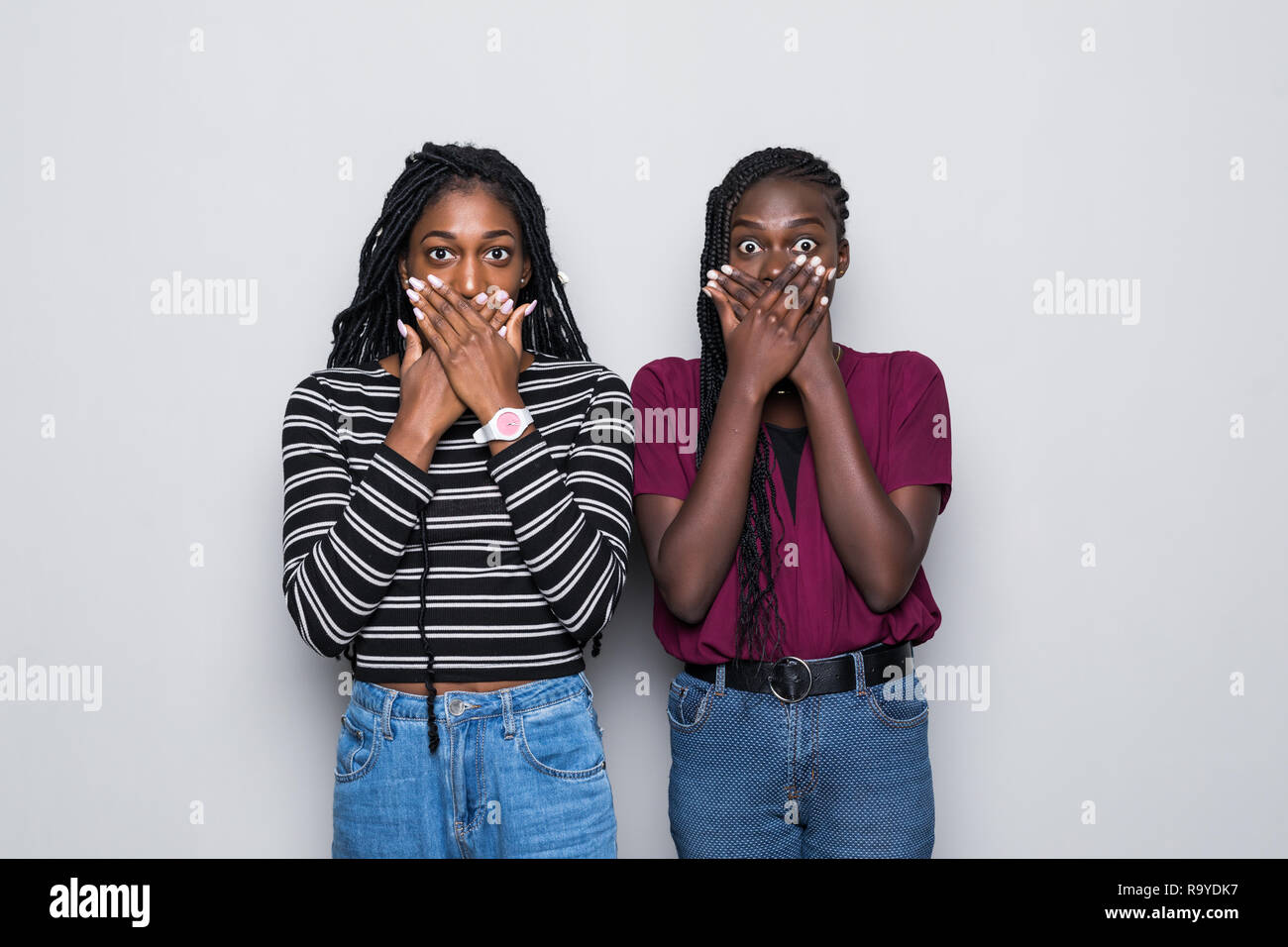 Waist up shot of shocked two african women cover mouthes with both ...