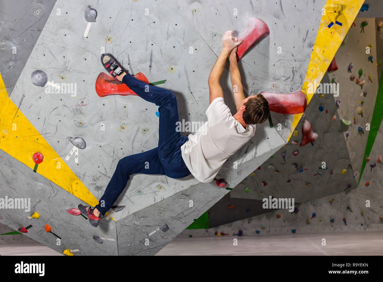 Rock climber man hanging on a bouldering climbing wall, inside on