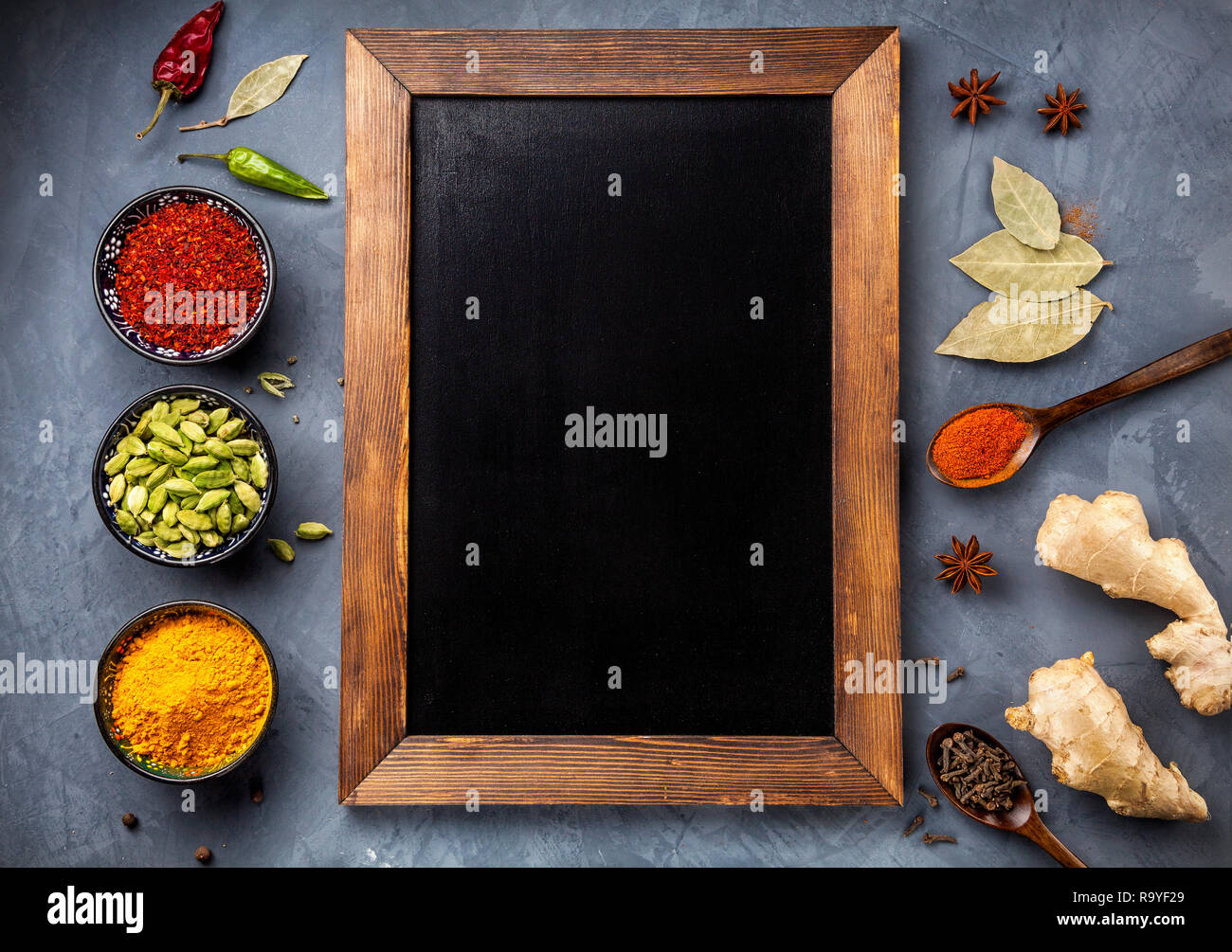 Various Spices like turmeric, cardamom, chili, paprika, ginger, star anise and clove near blackboard on grunge background. Free space for your text Stock Photo