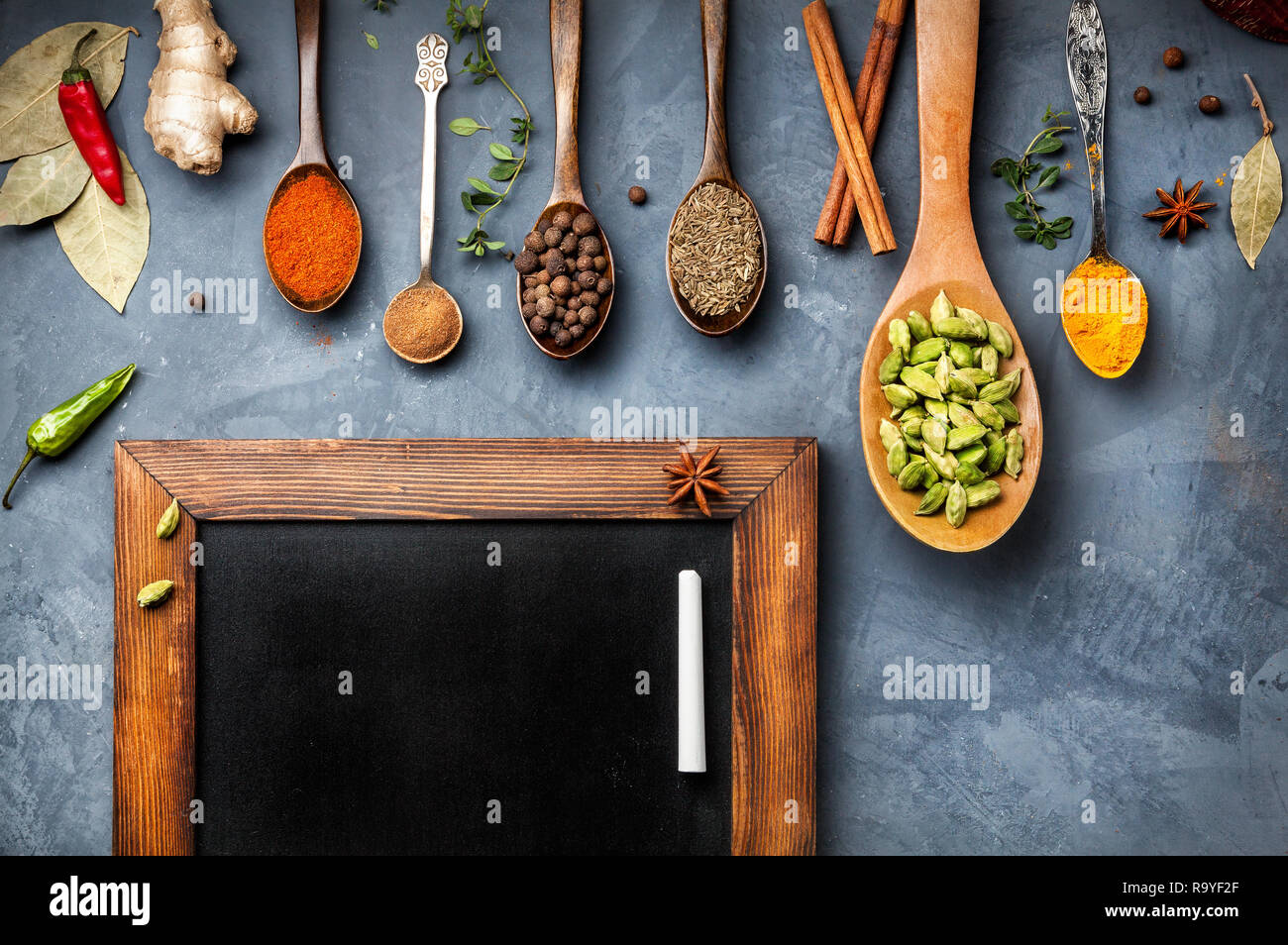Various Spices like turmeric, cardamom, chili, ginger, star anise and cinnamon near blackboard on grunge background. Free space for your text Stock Photo
